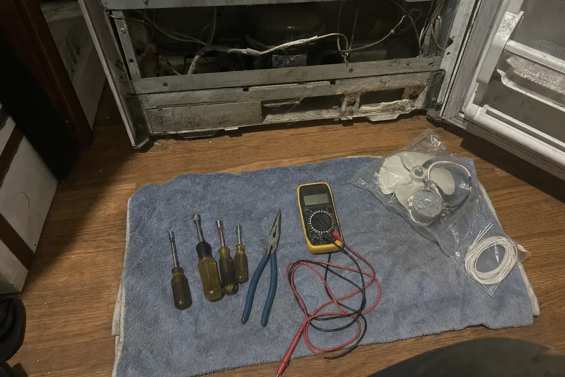 Flat-lay of nut drivers, pliers, a multimeter and a bagged fan motor on a towel - Built-In and Integrated Dishwasher Repair
