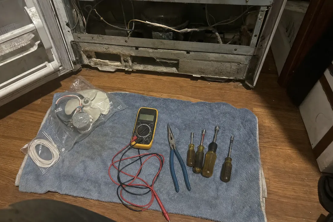 Flat-lay of nut drivers, pliers, a multimeter and a bagged fan motor on a towel, the multimeter in frame - Built-In Refrigeration Repair