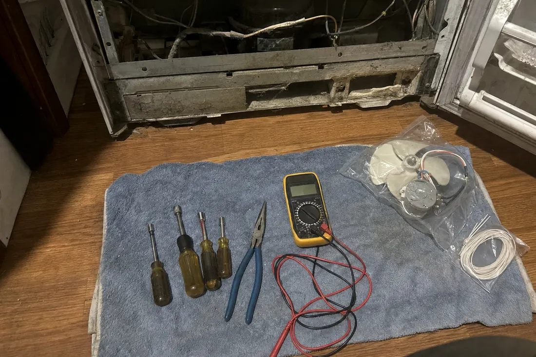 Flat-lay of nut drivers, pliers, a multimeter and a bagged fan motor on a towel, the folded towel in frame - Where we cover