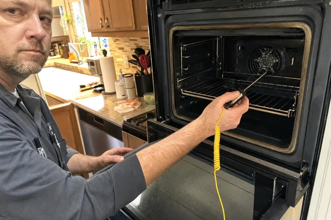 Technician holding a probe thermometer inside an open wall oven, the oven racks in frame - Steam Oven and Built-In Coffee System Repair