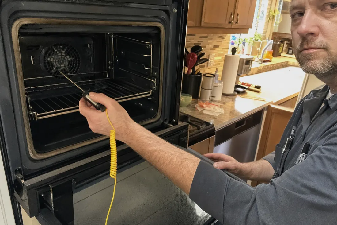 Technician holding a probe thermometer inside an open wall oven, the kitchen behind in frame - Questions we are asked most