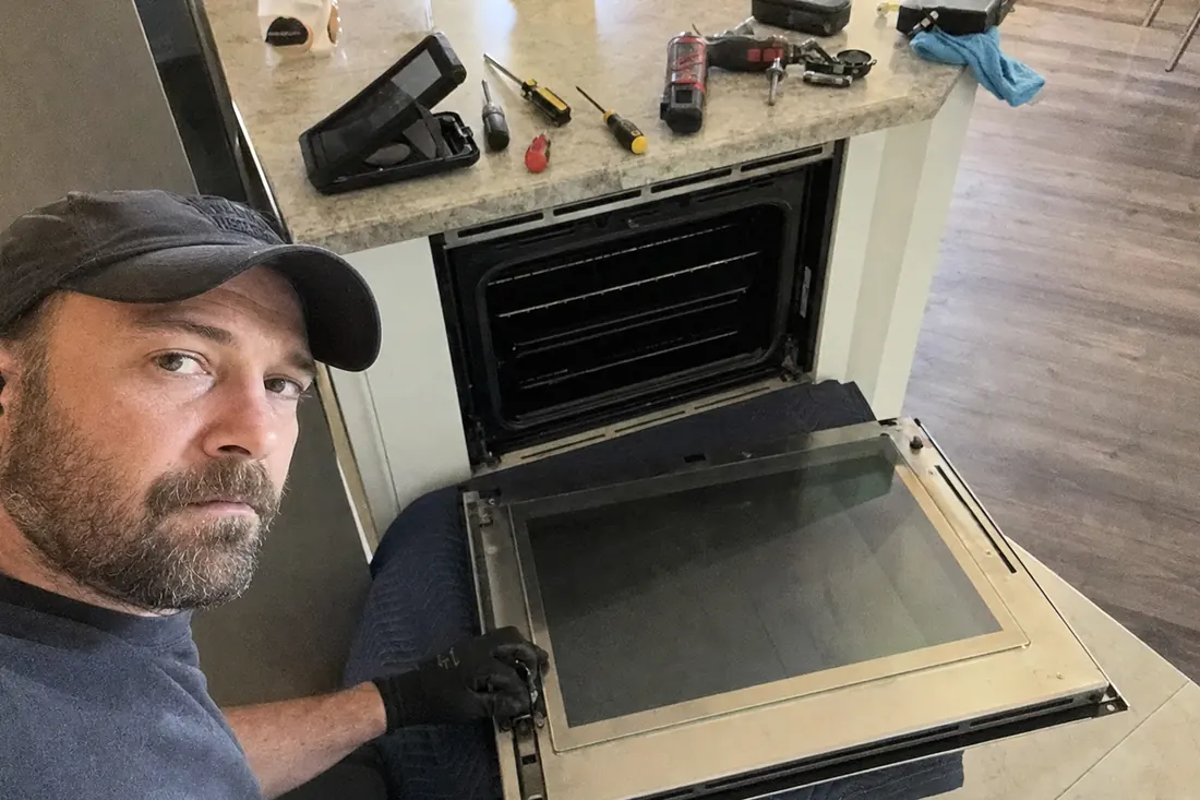 A wall oven door off its hinges on a moving blanket, hinge mechanism exposed, the moving blanket in frame - Brands we service