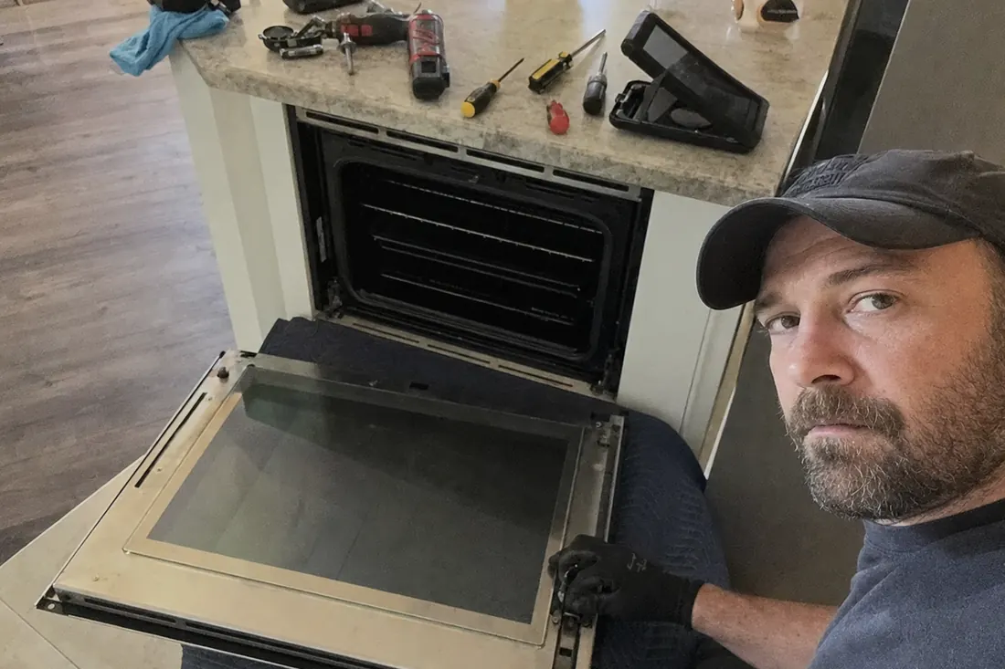 A wall oven door off its hinges on a moving blanket, hinge mechanism exposed, the empty oven opening in frame - Appliance Repair in St. Johns County